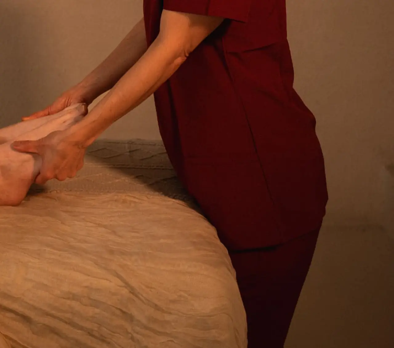 A practitioner in wine linen resting both hands over a woman feet under a soft folded blanket