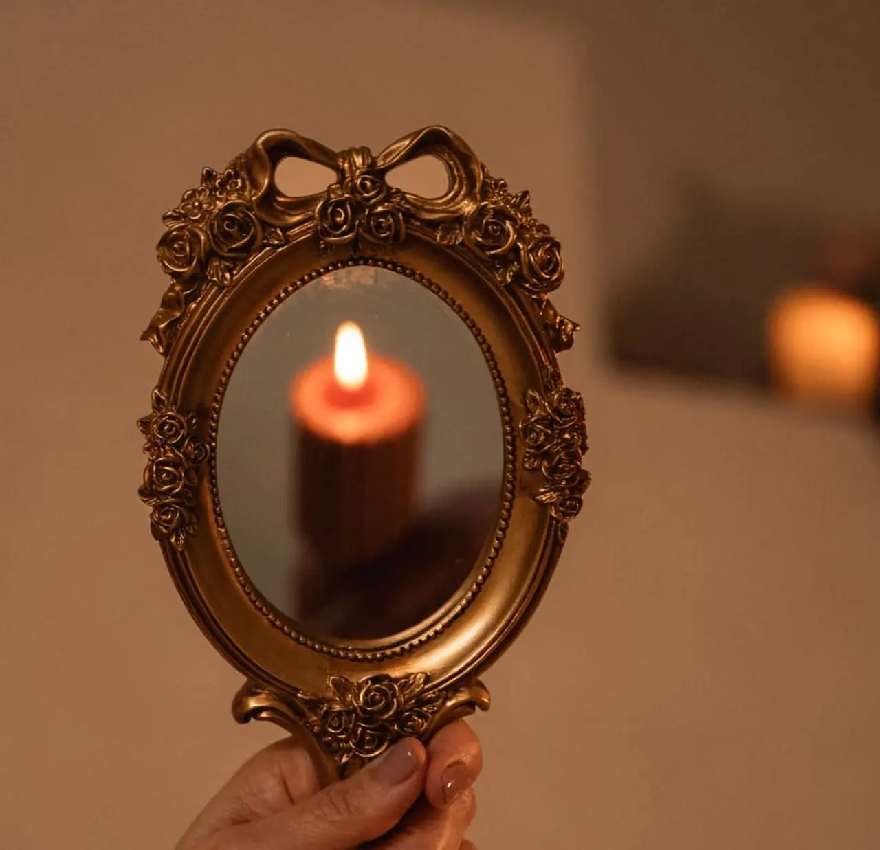 A single candle flame reflected in an ornate gold hand mirror against a warm plaster wall