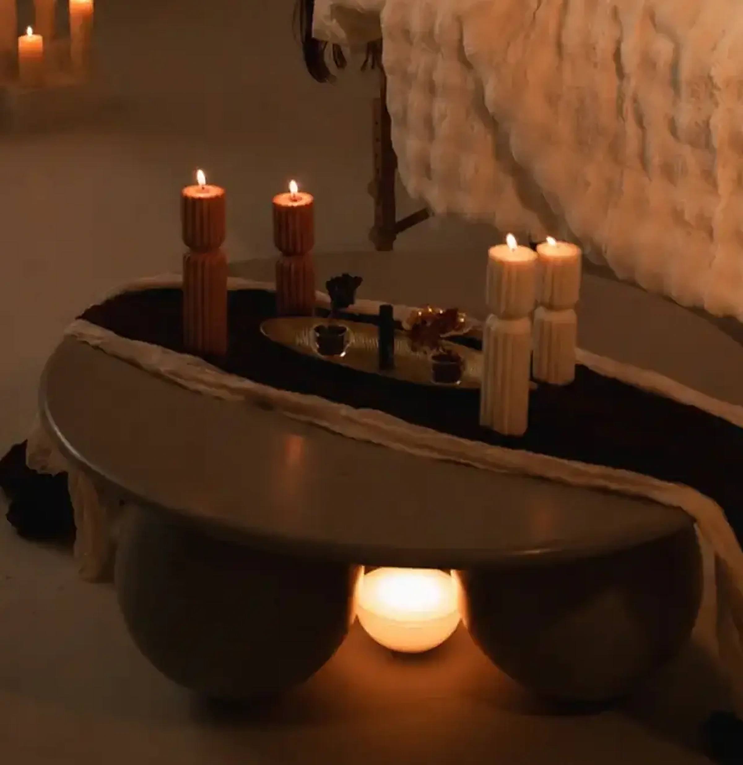 Ribbed candles burning beside a dark stone bowl of water with a low flame glowing beneath it