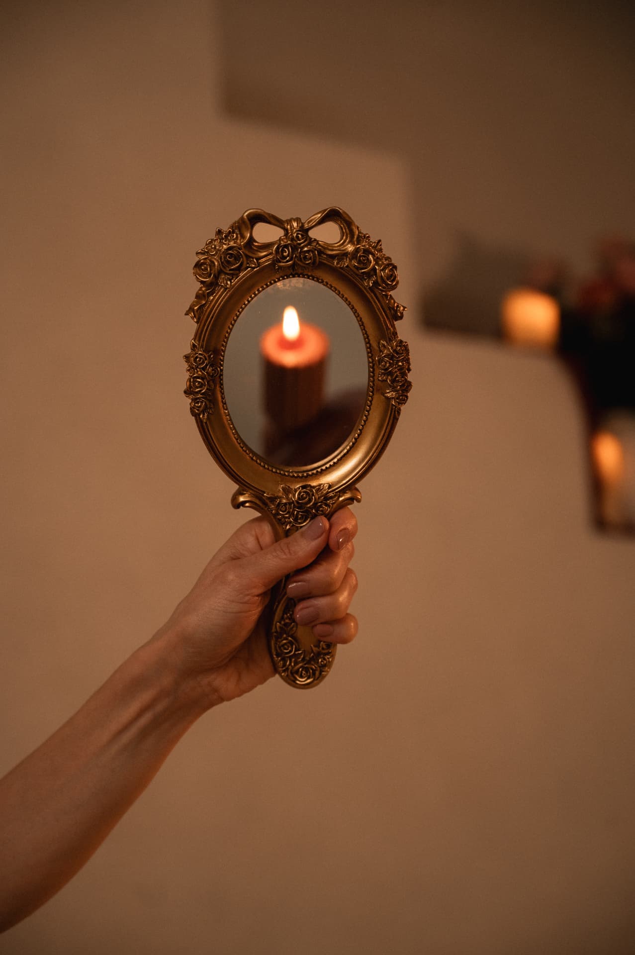 A hand holding an ornate gold mirror that reflects a single burning candle flame