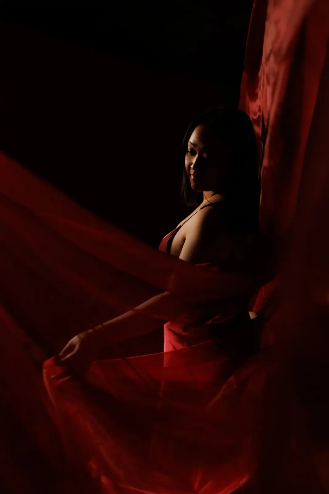 A woman in red silk turning through sheer crimson fabric in near darkness